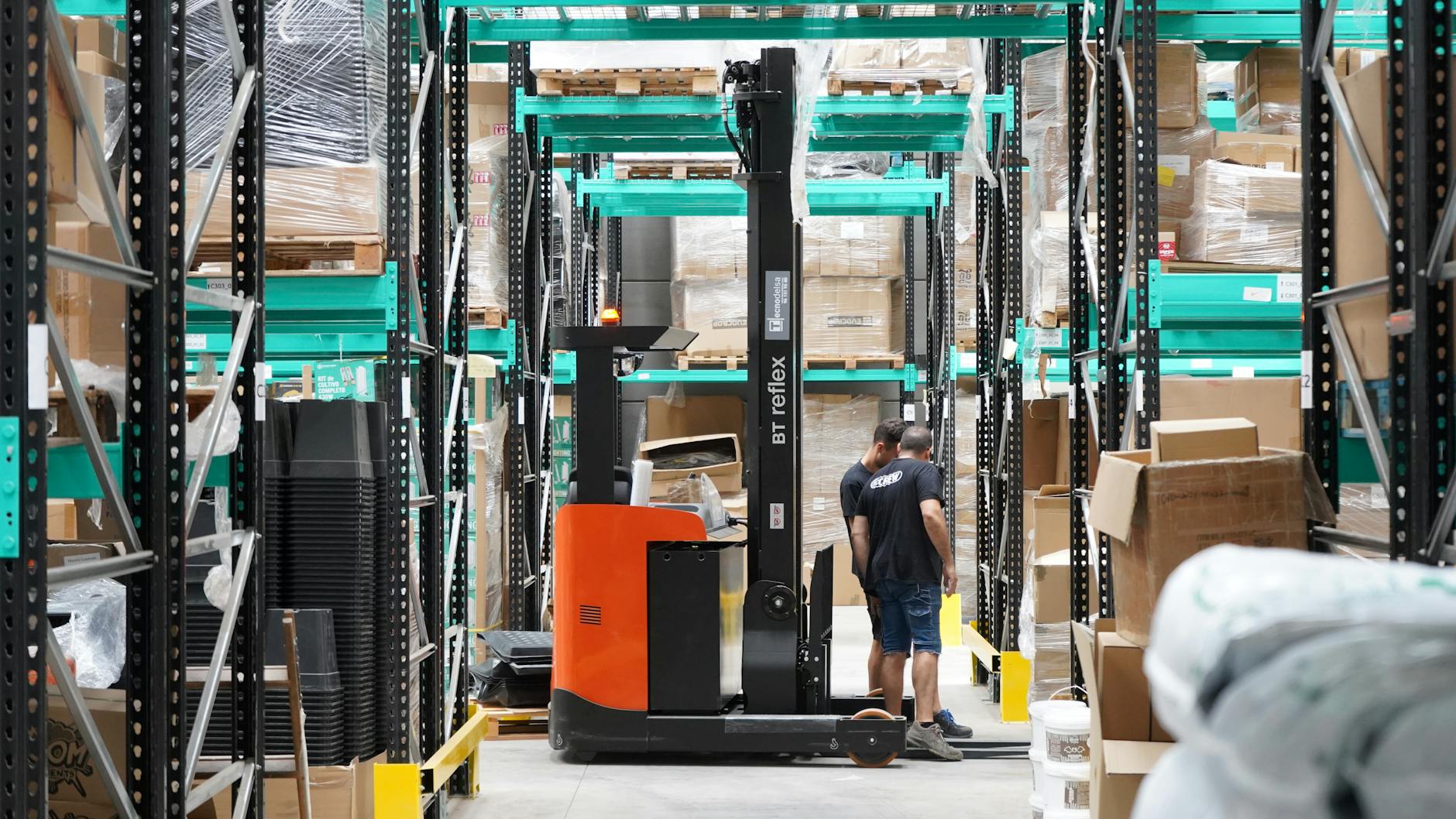 Pracownicy w magazynie e-commerce między regałami z użyciem wózka widłowego
