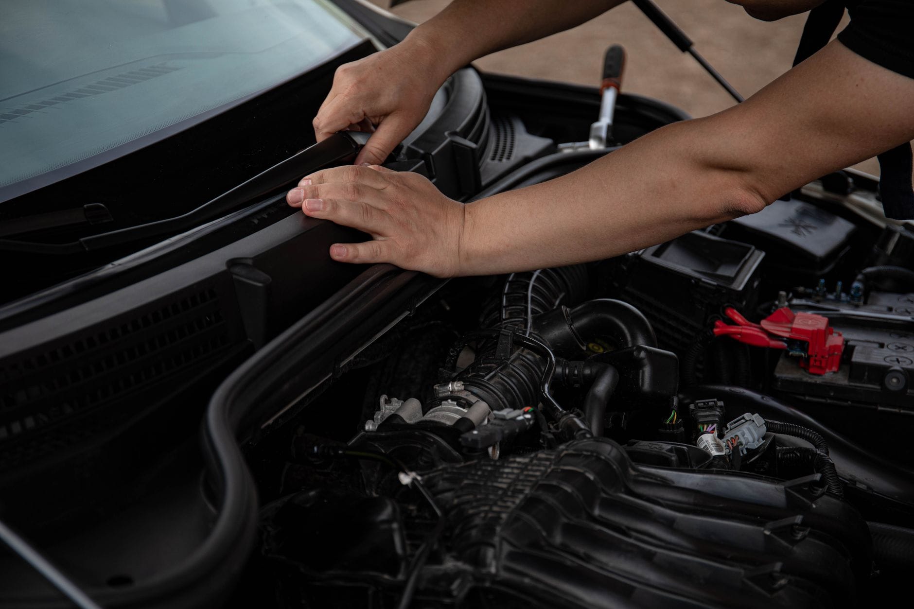 Dłonie mechanika naprawiające wycieraczkę przy otwartej masce auta