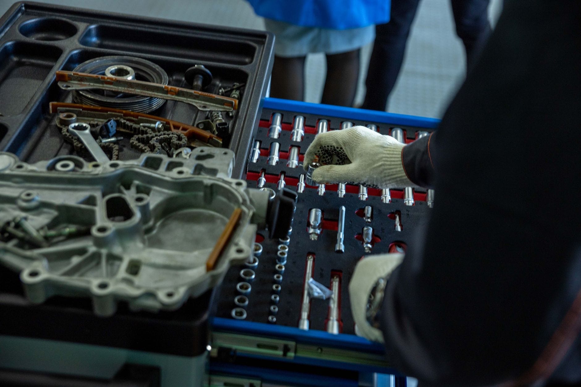 Mechanik w rękawiczkach układa części silnika i narzędzia w warsztacie