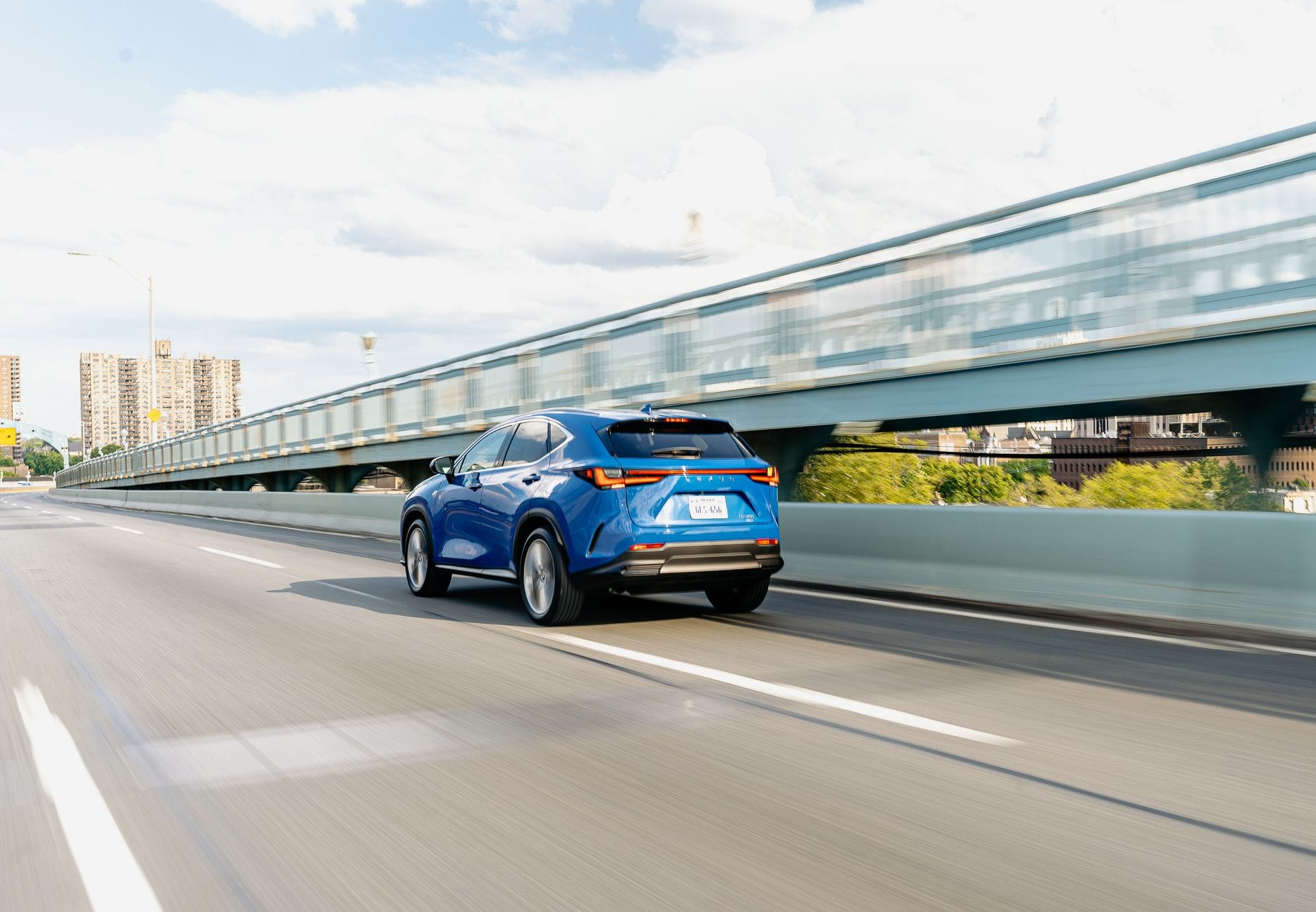Niebieski crossover Renault jedzie szybko po miejskim moście w słońcu