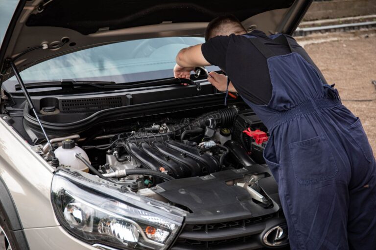 Mechanik w niebieskim kombinezonie pracuje przy silniku samochodu na zewnątrz